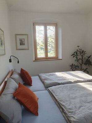 A bedroom with two beds, a window with a view of trees, a wall-mounted lamp, and a framed picture.