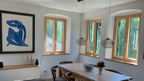 A dining area with a wooden table, chairs, pendant lights, and a framed artwork on the wall.