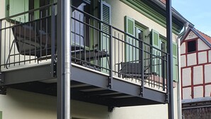 A balcony with metal railings, a green door, and a red roof.