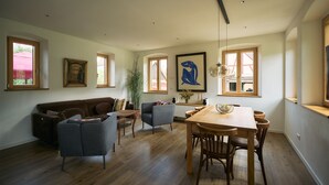 A modern living room with a sofa, armchairs, a dining table, and a large window.