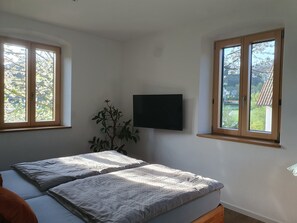 Quarto com duas camas, televisão e janela com vista para árvores.
