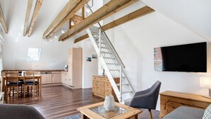 A spacious living area with a wooden staircase, a dining set, and a flat-screen TV. - Apartment 'Fewo 1' with Balcony and Wi-Fi (Koserow)