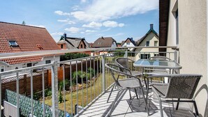 A balcony with a glass table and wicker chairs, overlooking a garden and neighboring houses. - Apartment 'Fewo 1' with Balcony and Wi-Fi (Koserow)