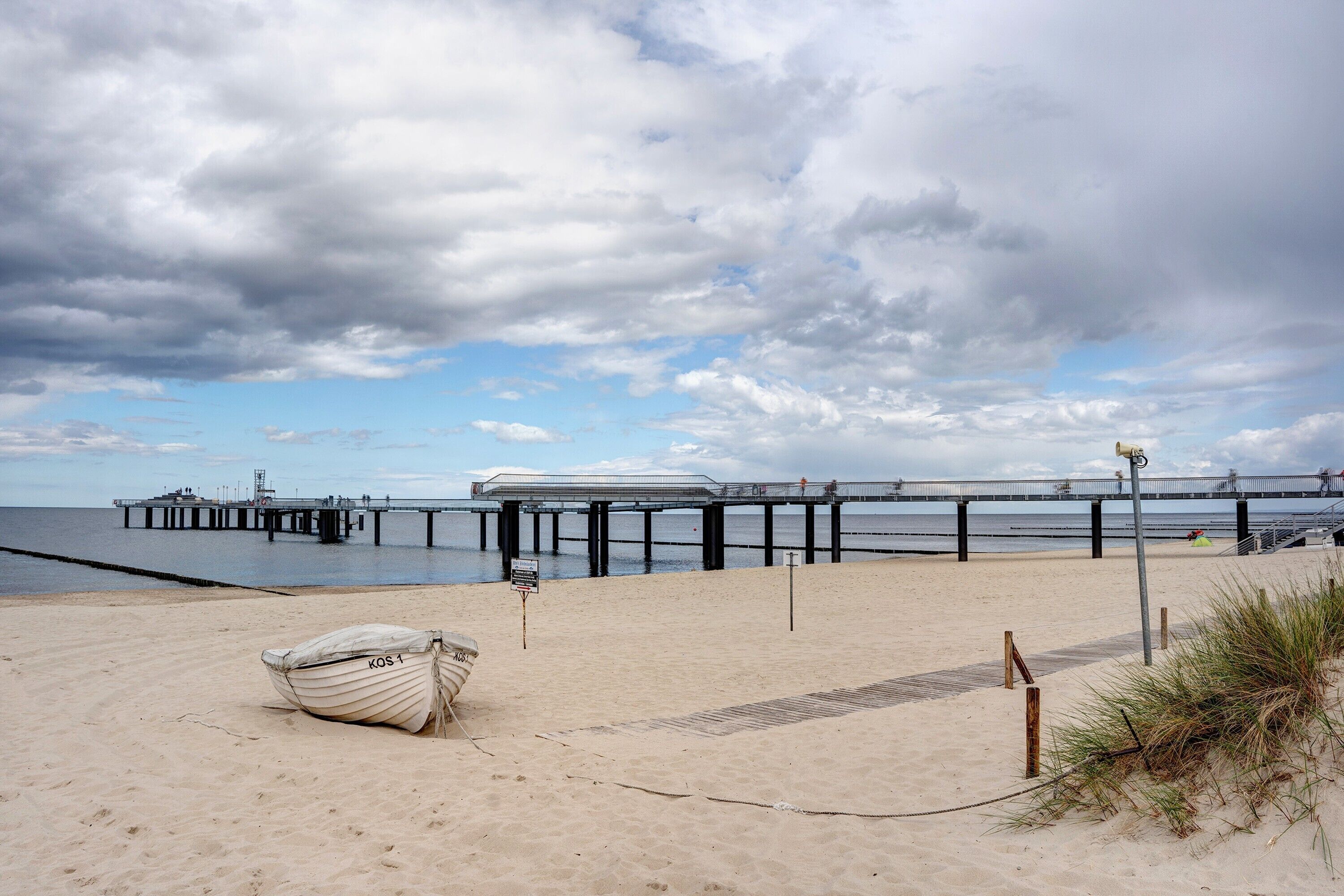 A beach with a boat, a pier, and a cloudy sky.