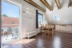 A modern kitchen with wooden beams, a dining area with chairs, a window with a view, and a balcony with a table and chairs.
