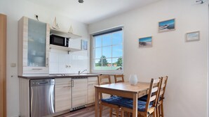 A modern kitchen with a dishwasher, microwave, and wooden cabinets. There is a dining table with chairs and a window with a view of the outside. - Apartment 'Fewo 2' with Balcony and Wi-Fi (Koserow)