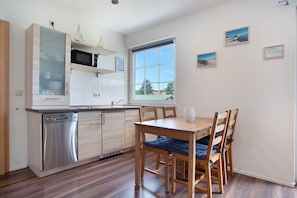 A modern kitchen with a dishwasher, microwave, and wooden cabinets. There is a dining table with chairs and a window with a view of the outside. - Apartment 'Fewo 2' with Balcony and Wi-Fi (Koserow)