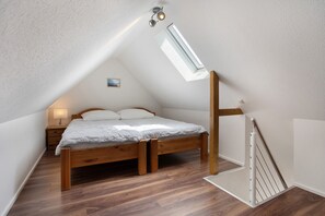 A bedroom with a sloped ceiling, a bed, a nightstand, a lamp, and a skylight.