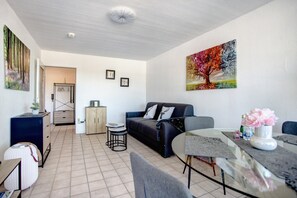 A modern living room with a sofa, coffee table, and dining table. There is a painting on the wall and a door leading to another room. - Apartment 'The View' with Mountain View, Balcony and Wi-Fi (Bad Reichenhall)