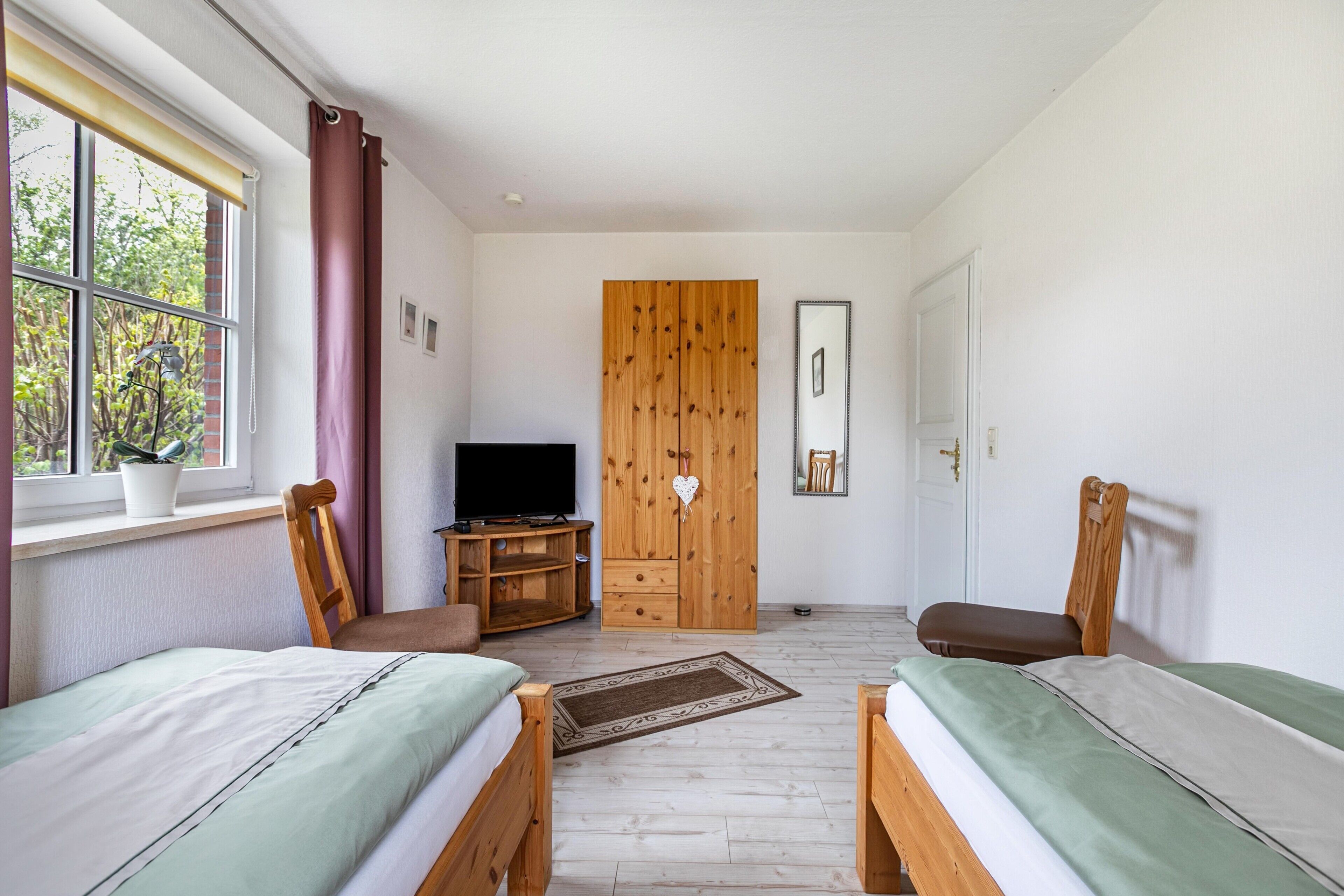 A bedroom with two beds, a TV, a wardrobe, and a window with curtains.
