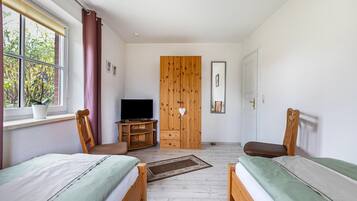 A bedroom with two beds, a TV, a wardrobe, and a window with curtains.