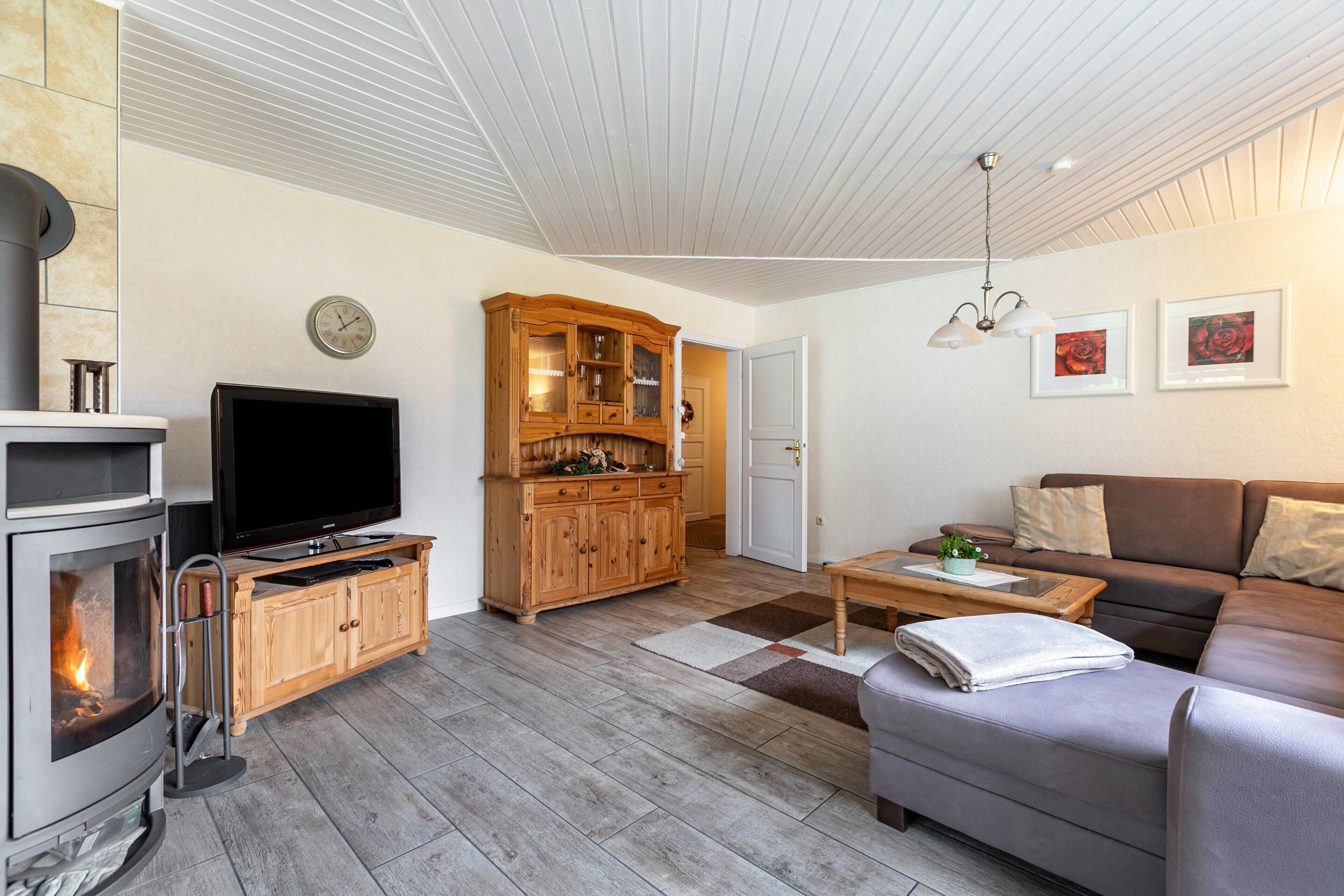Een woonkamer met een open haard, televisie, houten kast, bank en kunst aan de muur.