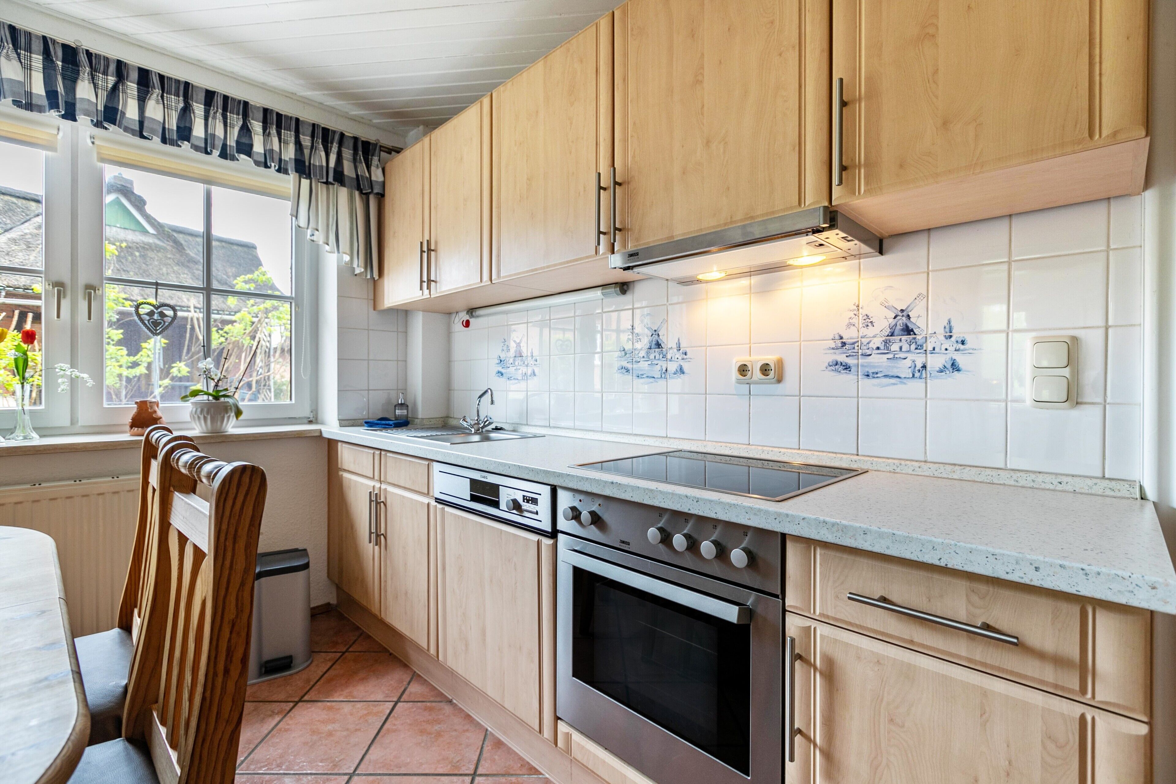 Een keuken met houten kasten, een fornuis, een vaatwasser en een raam met uitzicht op een huis.