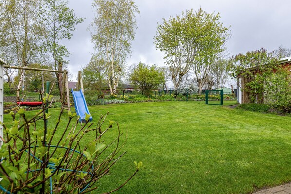 A well-maintained backyard with a slide, a fenced play area, and mature trees.