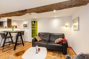 Una sala de estar moderna con techo de madera, un sofá de cuero negro, una mesa de centro blanca y una zona de comedor con una estantería verde.