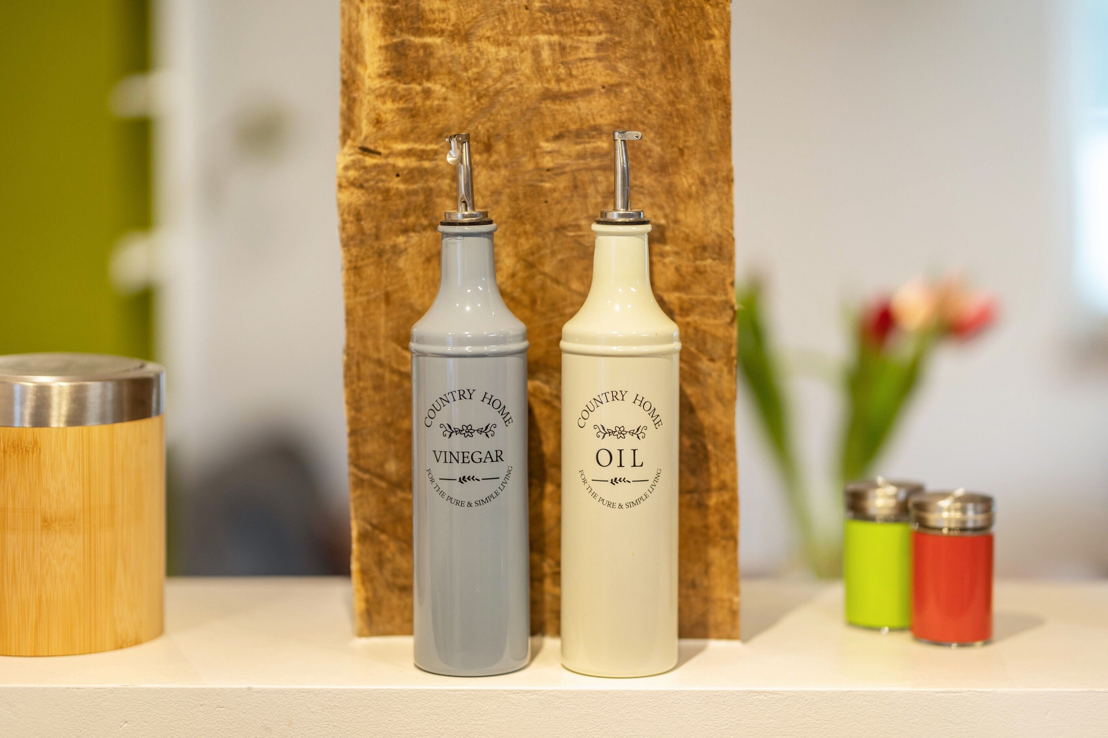 Deux bouteilles étiquetées « vinaigre de la marque Country Home » et « huile de la marque Country Home » sont posées sur une étagère.