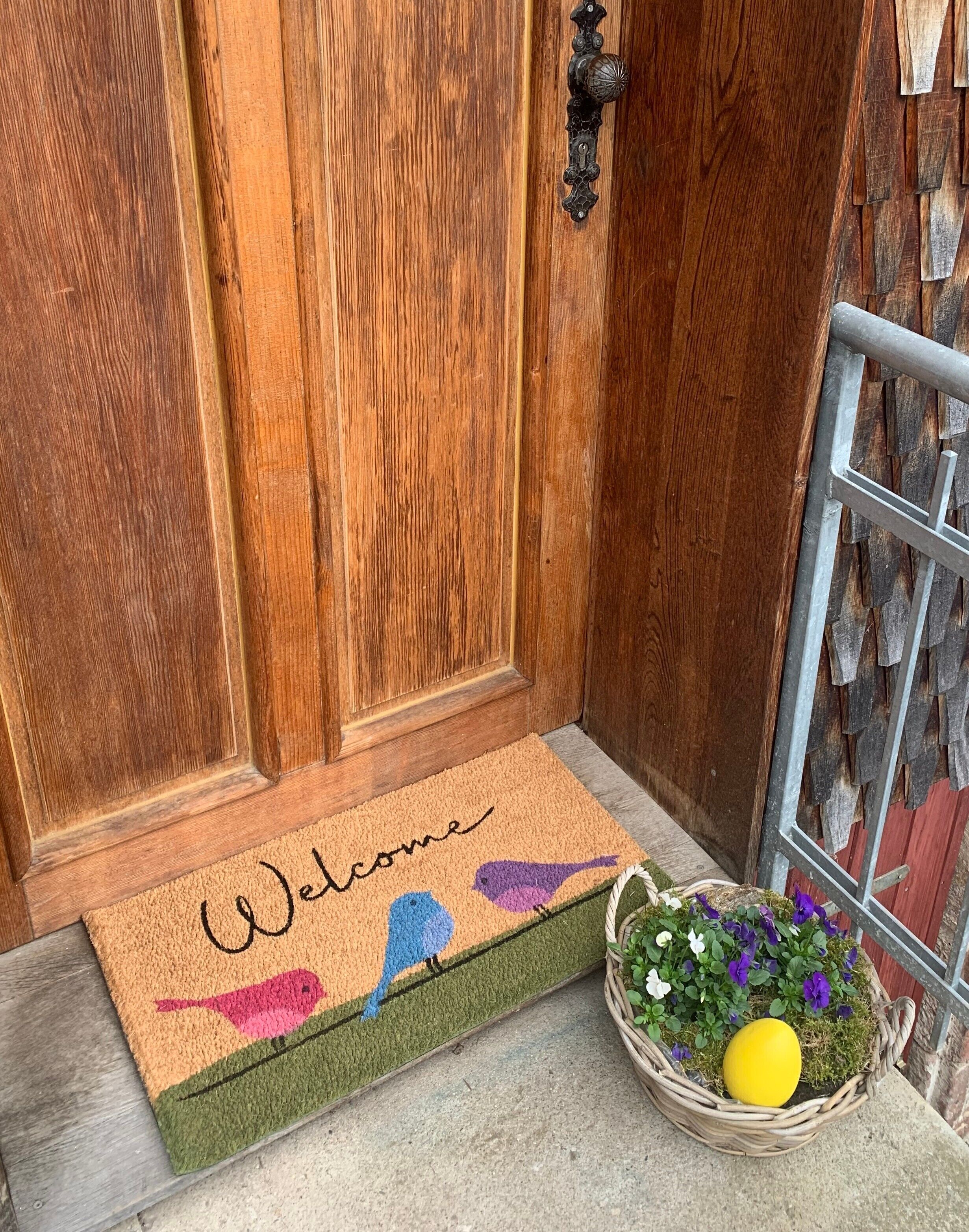 A wooden door with a doormat that reads 'Welcome' and a basket with flowers.
