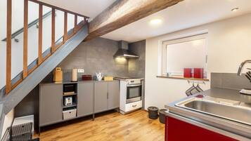 Una cocina con escalera de madera, armarios grises, un lavamanos de acero inoxidable y una ventana con cortinas rojas.
