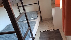 Ein Etagenbett mit grauer Bettwäsche, einer gewebten Matte und einem Badezimmer mit Waschbecken in Weiß und orangefarbenen Vorhängen.