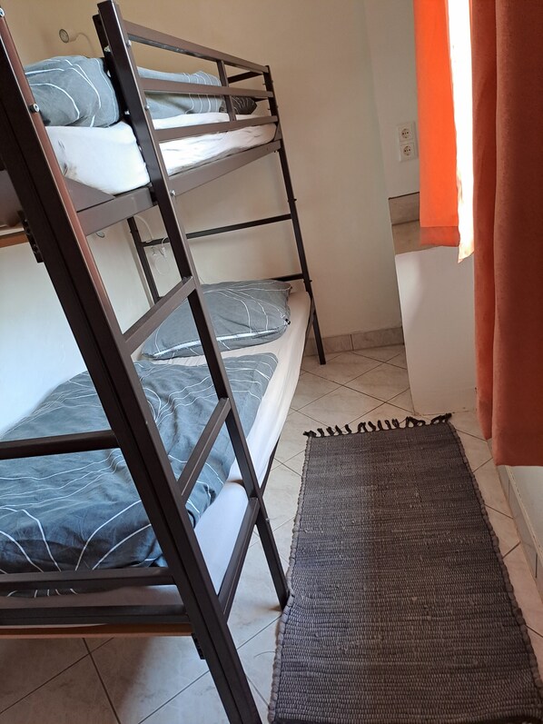 A bunk bed with grey bedding, a woven mat, and a bathroom with a white sink and orange curtains. - Apartment 'Hof Gerbert' with Shared Garden and Wi-Fi (Halenbeck-Rohlsdorf)