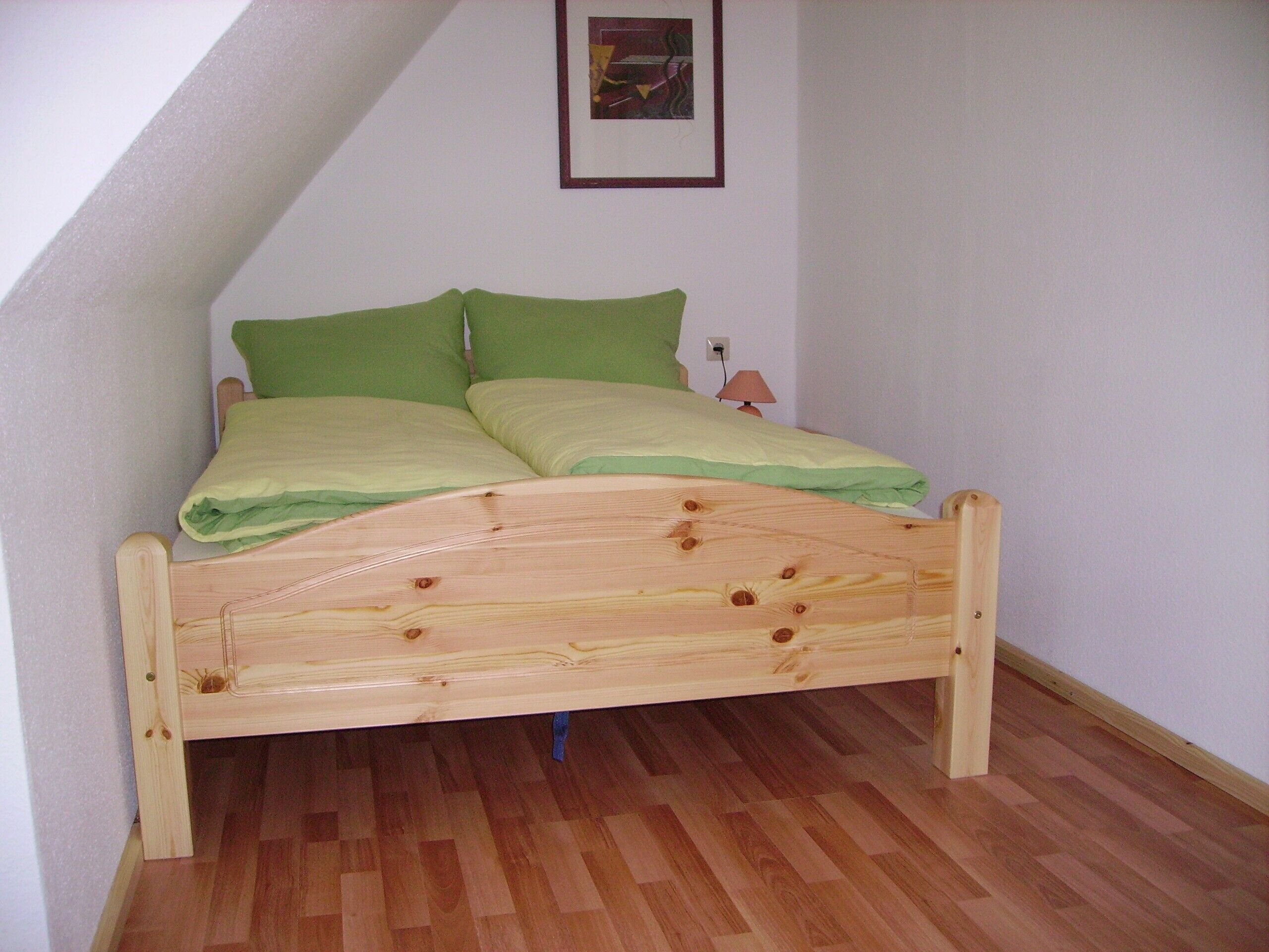 Ein Bett mit Holzbettgestell und grüner Bettwäsche in einem Zimmer mit Holzboden und einer weißen Wand.