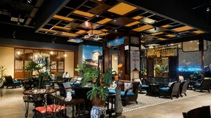 Ein Restaurant mit modernem Ambiente, das eine Mischung aus Holz- und Metallmöbeln, einem Fliesenboden und einer Decke mit geometrischem Muster zeigt.