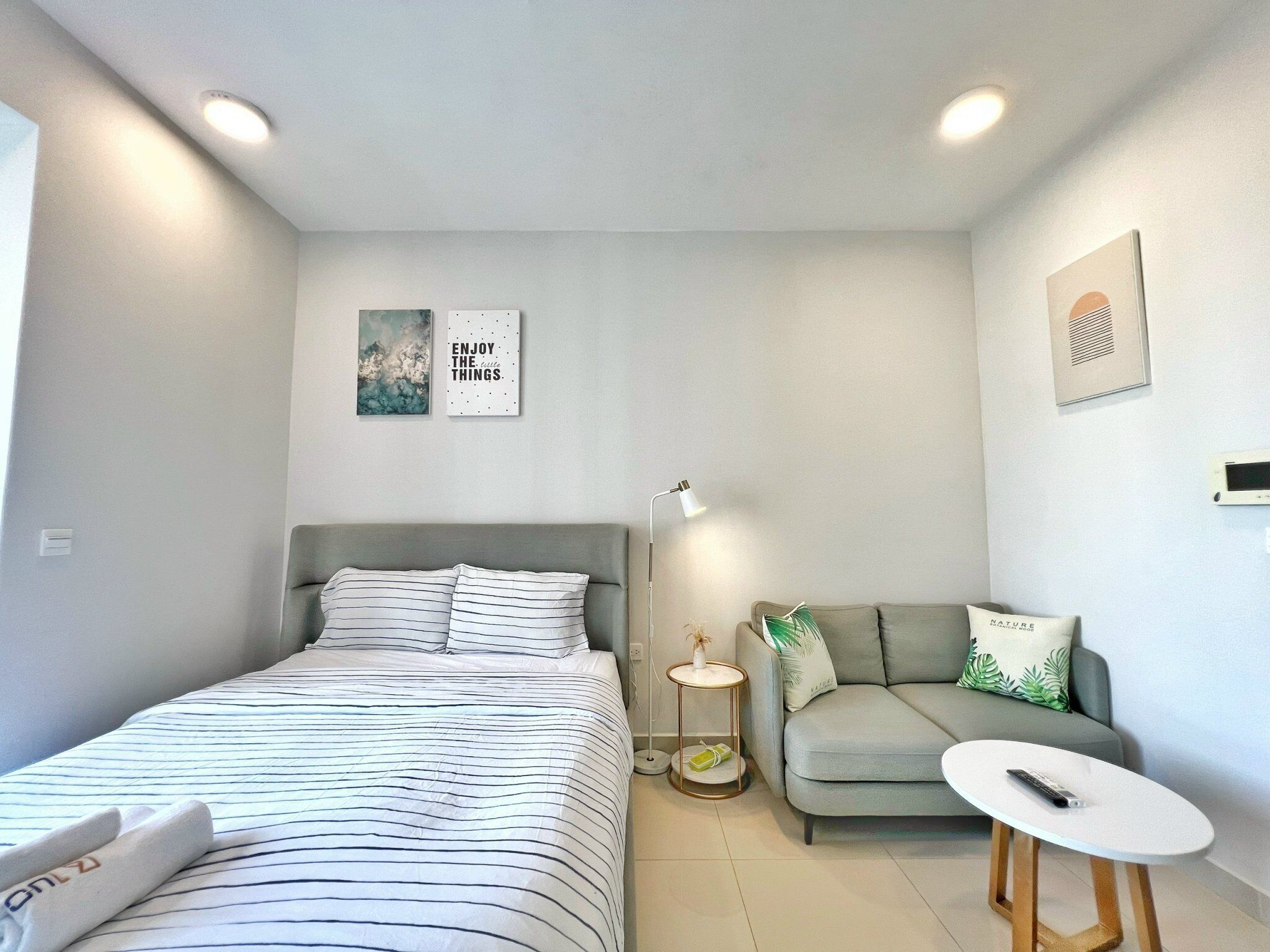 A modern, well-lit bedroom with a bed, a small sofa, a round table, and a nightstand.