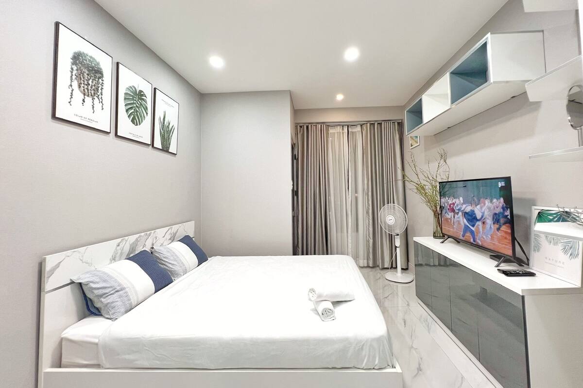 A modern bedroom with a bed, a TV, and framed botanical prints on the wall.