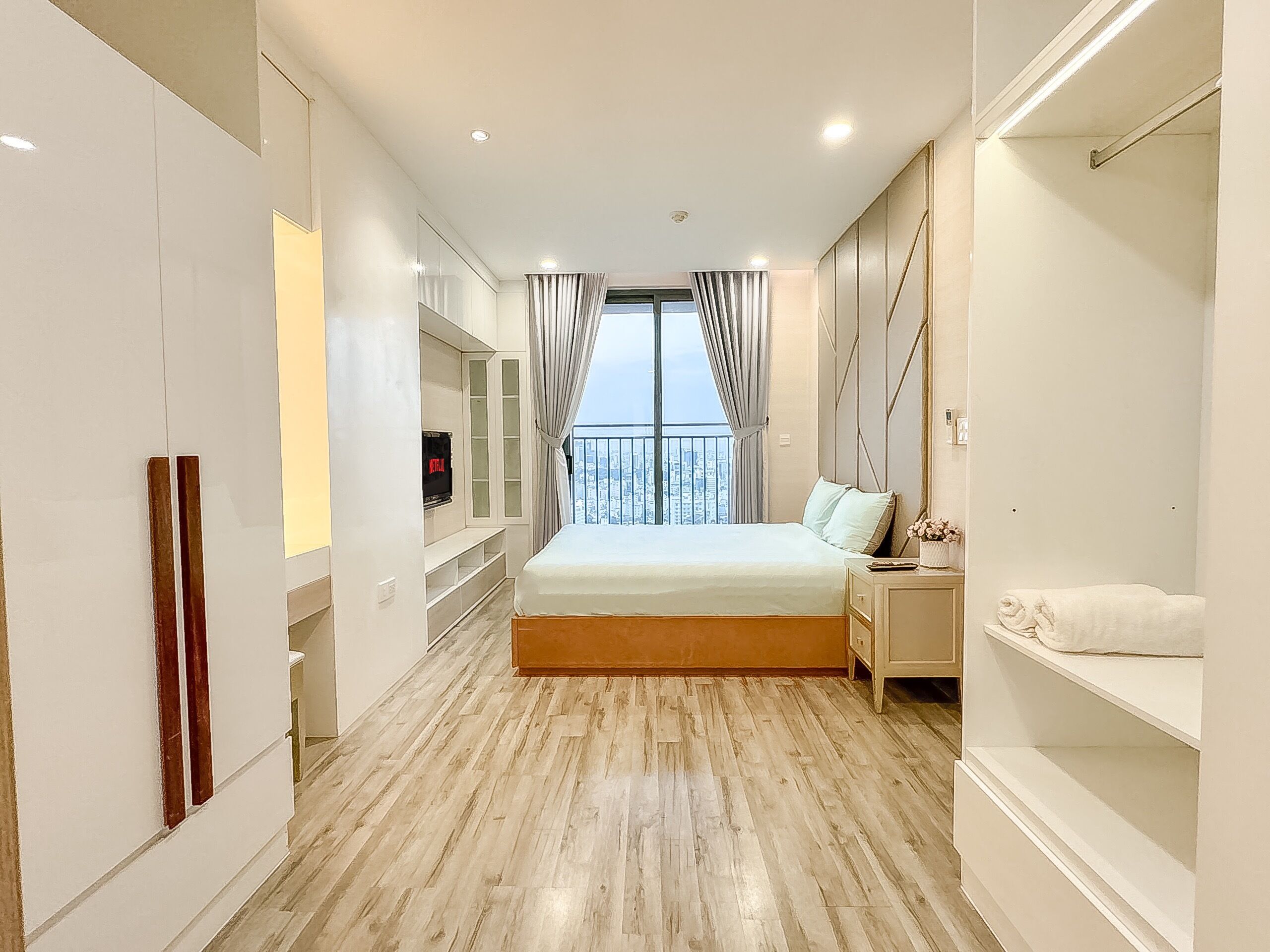 Una habitación de hotel moderna con una cama grande, armario empotrado, televisión y balcón con vistas a la ciudad.