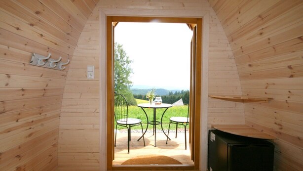 Un intérieur en bois avec une porte donnant sur un espace extérieur aménagé avec deux chaises et une table.