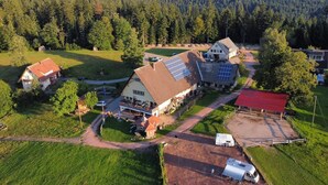 Vue aérienne d’une propriété rurale comprenant une maison principale, des panneaux solaires, une grange et de la végétation luxuriante.