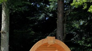 Une cabane en bois avec deux chaises et une table, entourée d’herbe et d’arbres.