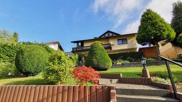 A two-story house with a balcony, surrounded by well-maintained gardens and a clear sky.