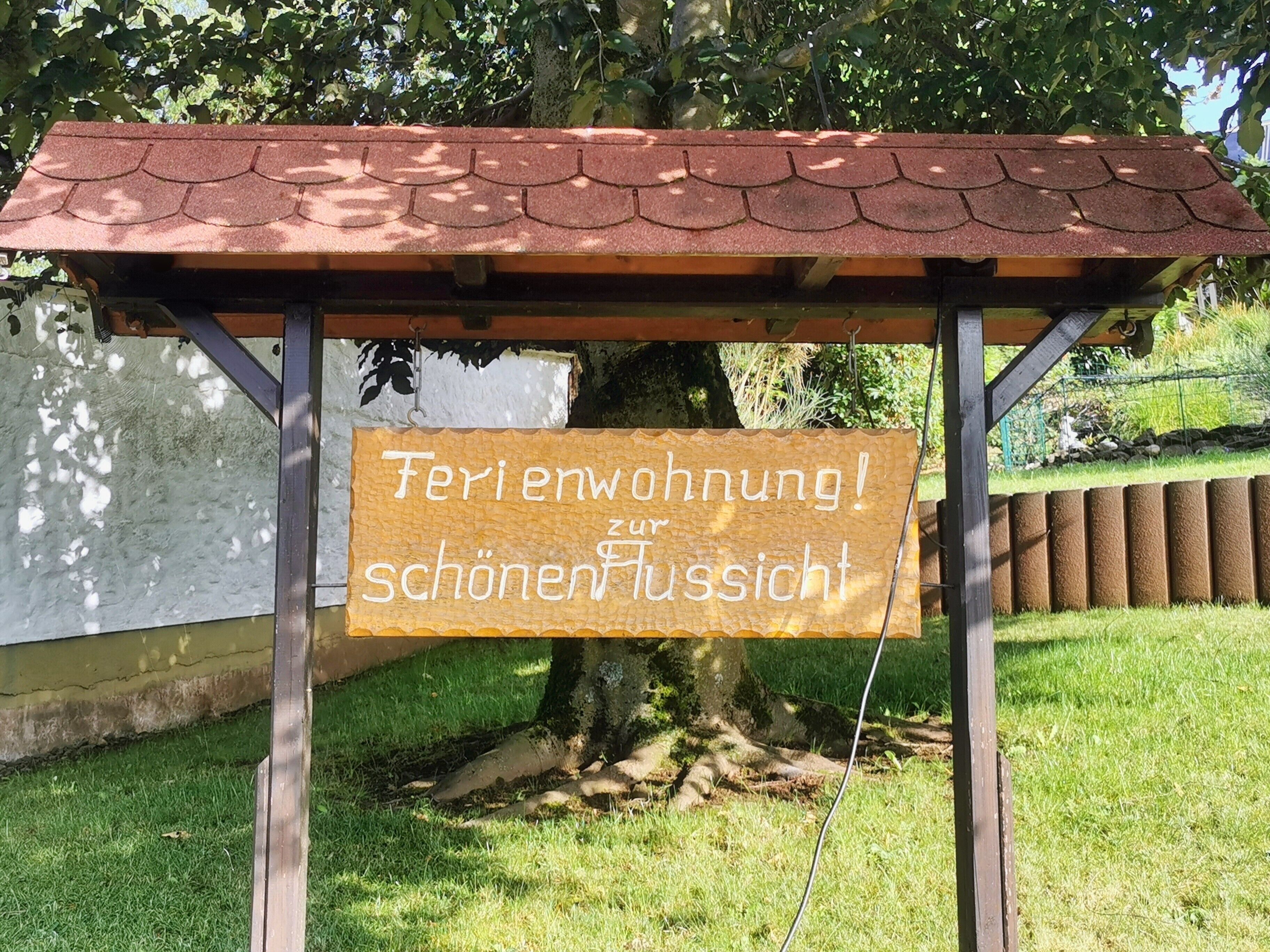 Una pèrgola amb un cartell que diu 'Ferienwohnung! zur schönen Aussicht' davant d'un arbre.
