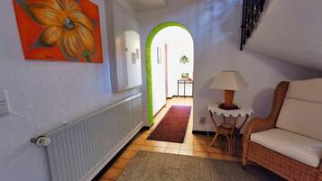 A hallway with a radiator, a wicker chair, a lamp, and a painting on the wall.
