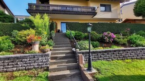 Una casa de dos pisos con un balcón, una puerta principal y un jardín con escalones que conducen a la entrada.