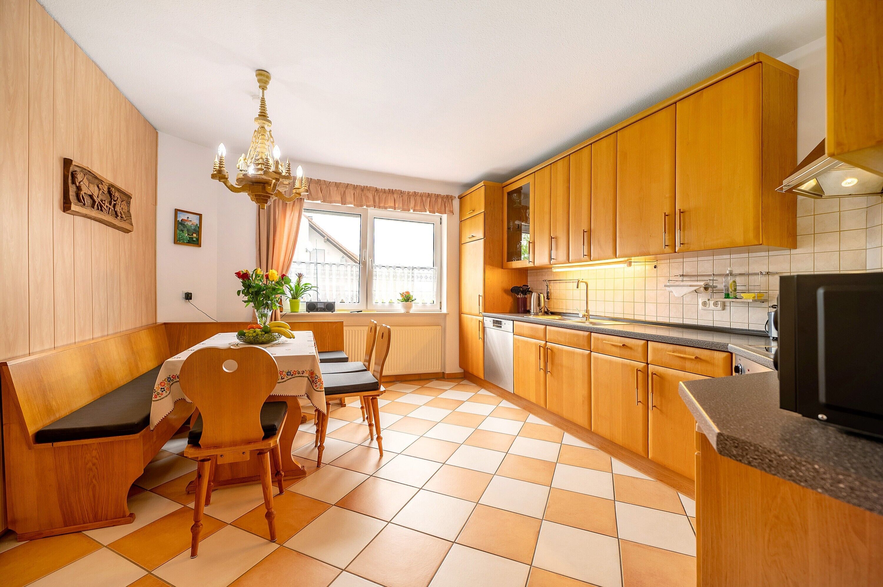 A kitchen with wooden cabinets, a dining table with chairs, a chandelier, and a window with curtains.