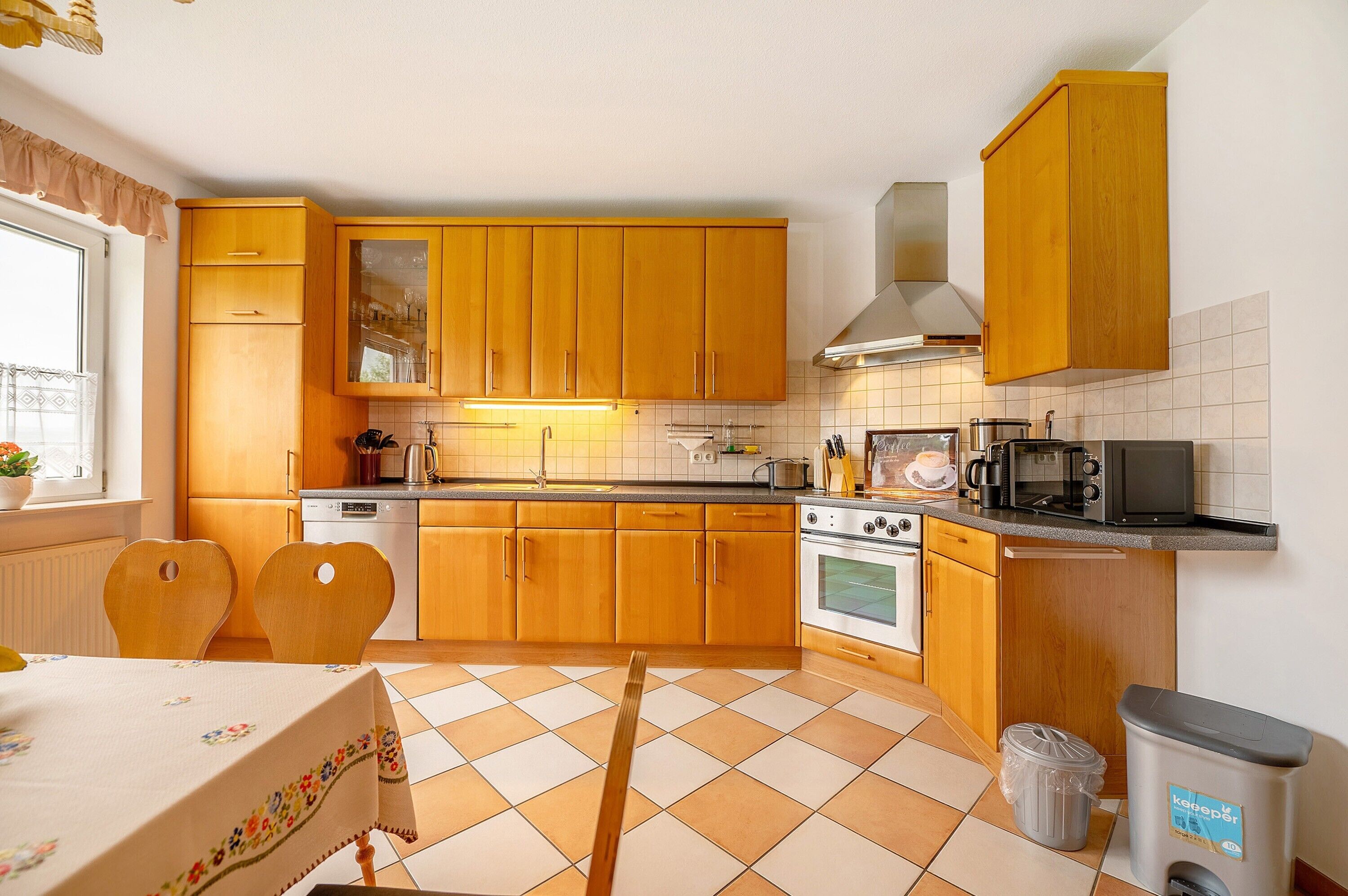 Een keuken met houten kastjes, een fornuis, een magnetron en een afvalbak.