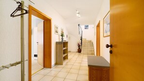 Un pasillo con una puerta de madera, un perchero, una escalera y un estante pequeño con un jarrón.