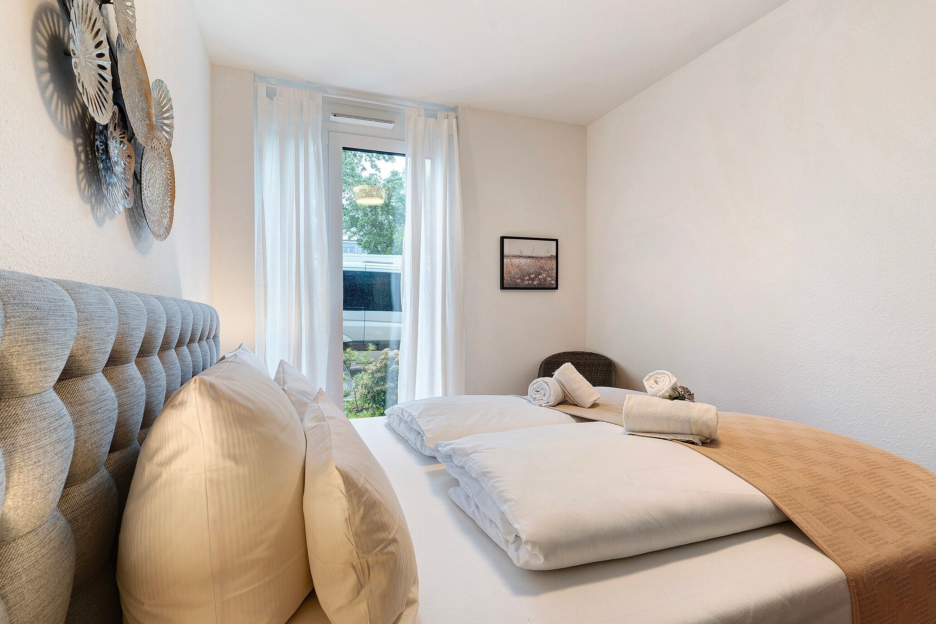 Ein Hotelzimmer mit einem großen Bett, einem fenster mit Vorhängen, einem Wandkunstwerk und einem gerahmten Bild.