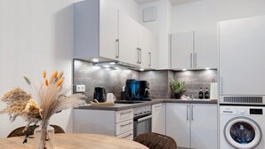 A modern kitchen with white cabinets, a built-in oven, a coffee maker, and a washing machine.