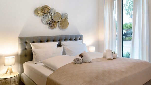 A neatly made bed with a grey upholstered headboard, white linens, and decorative wall art.