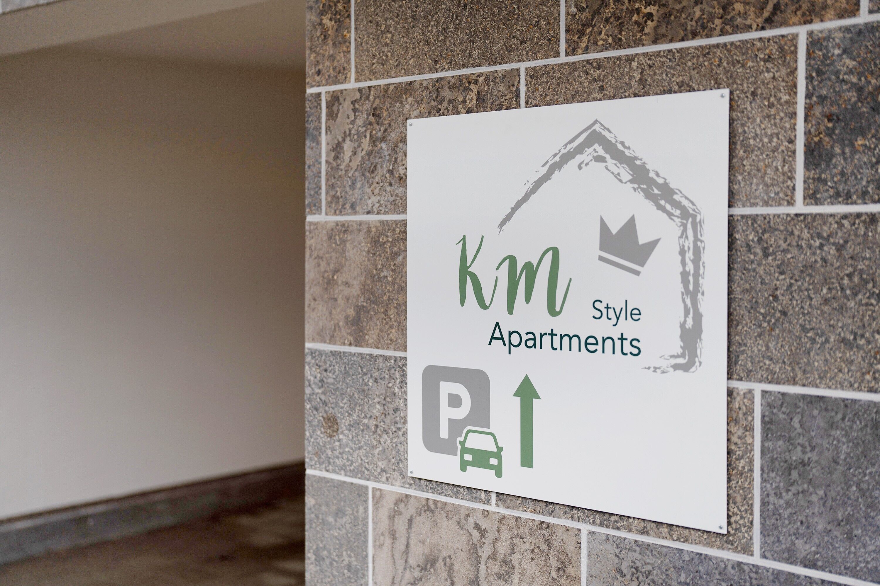 Opastekyltti, jossa lukee ”Km Style Apartments”, ja jossa on parkkisymboli sekä kruunukuvake.