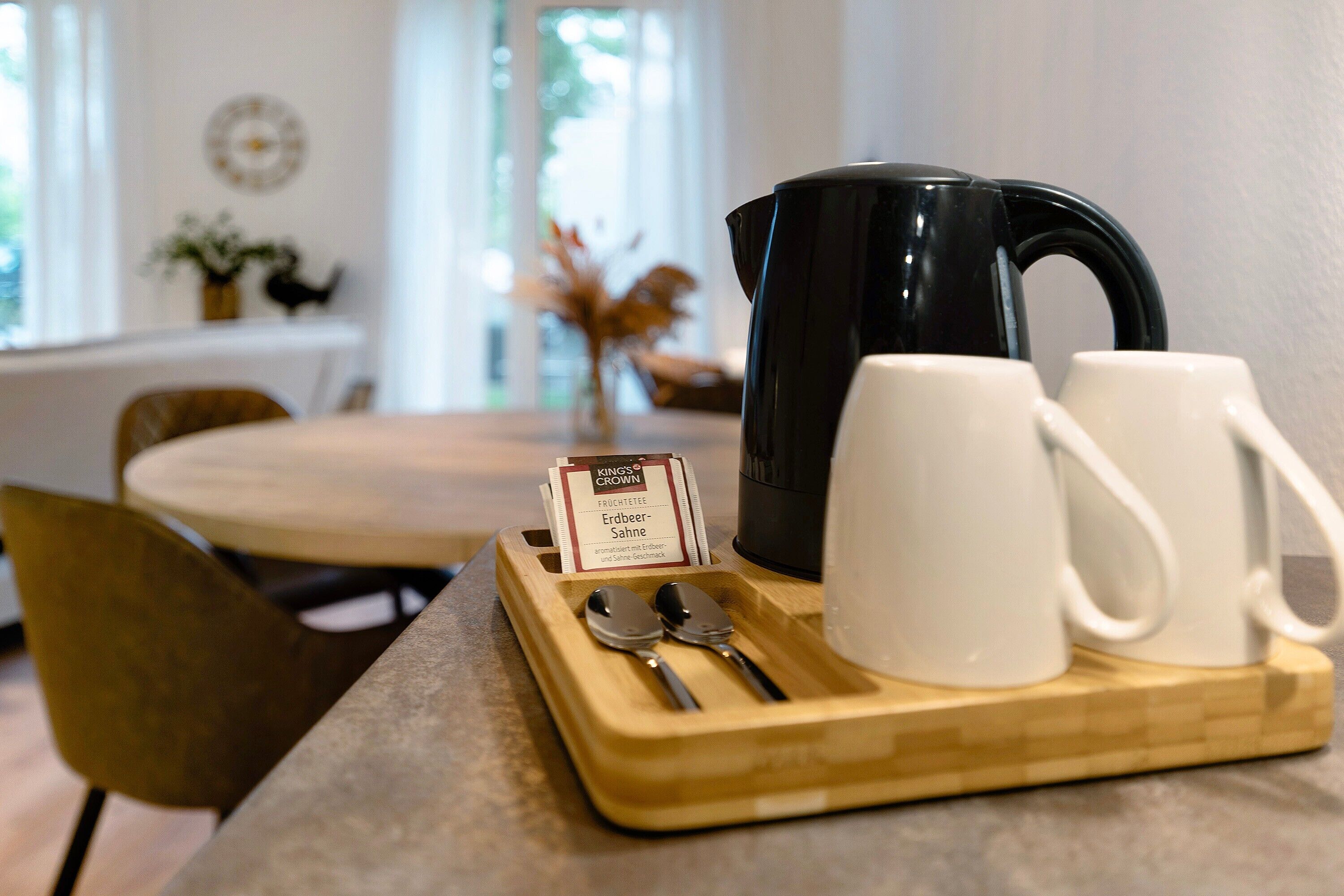 Ein Frühstücksbrett mit Kaffeekanne, zwei Tassen und einem Löffel auf einem Holztisch.