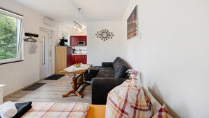 A compact living space with a sofa, a dining table, a kitchen area, and a large window.