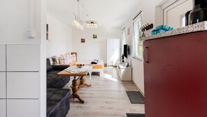 A modern kitchen with a red refrigerator, a dining area with a table and chairs, and a living room with a sofa.