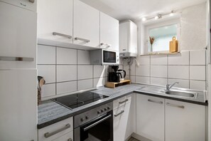 Una cocina moderna con armarios blancos, microondas integrado, estufa y pileta.
