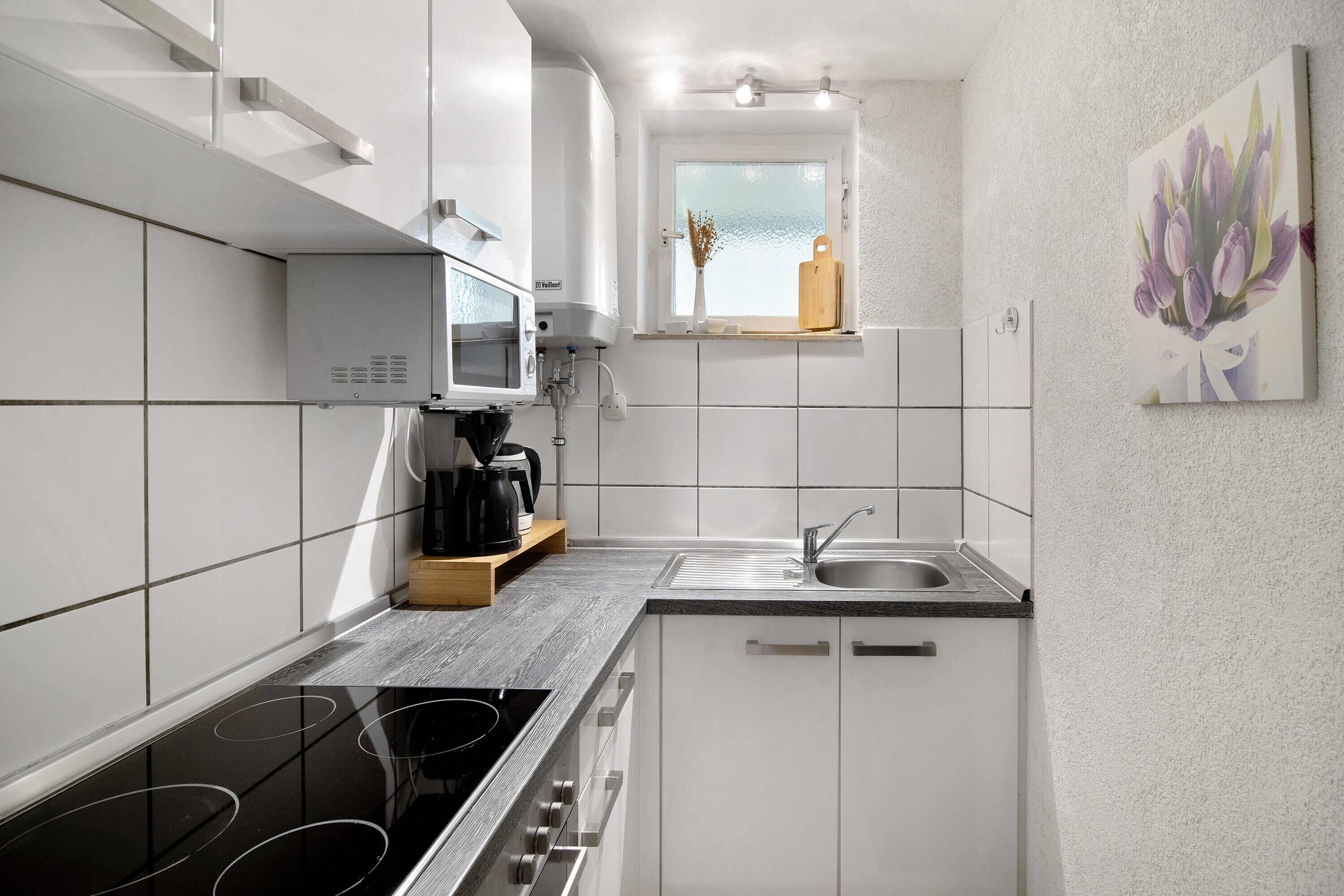 A modern kitchen with white cabinets, a black stove, a microwave, and a window with a view.