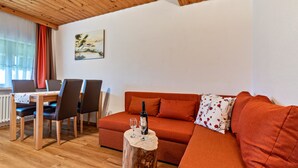 A cozy living room with a wooden ceiling, a red sofa, a wooden coffee table with a bottle and glass, and a dining area with chairs and a table. - Metzgerbauernhof Apartment with Shared Terrace, Garden, and Wi-Fi (Wolfach)