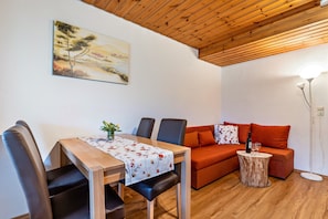 A dining area with a table, chairs, a sofa, a small side table, and a painting on the wall.